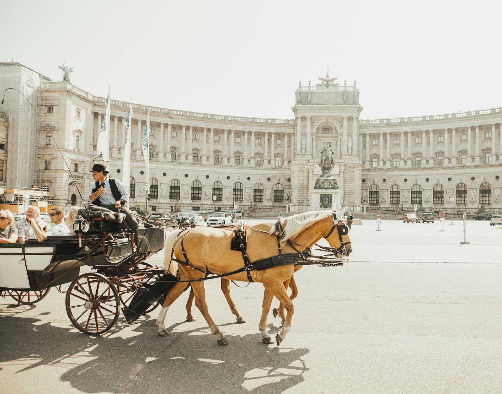 Eine Pferdekutsche mit Touristen vor der imposanten, geschwungenen Fassade der Hofburg an einem sonnigen Tag in Wien.