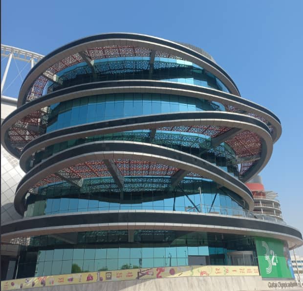Das 3-2-1 Qatar Olympic and Sports Museum in Doha: eine gestapelte Spirale aus Glas und weißen Terrassen mit dem 3-2-1-Logo an der Fassade unter klarem Himmel.