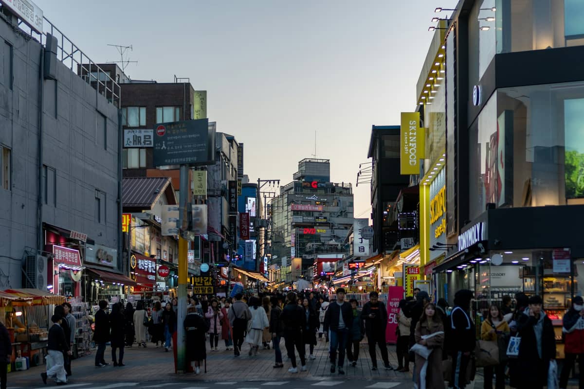 Rua pedonal movimentada em Seul, ladeada por lojas, cafés e letreiros, captando a atmosfera energética de um popular distrito comercial.
