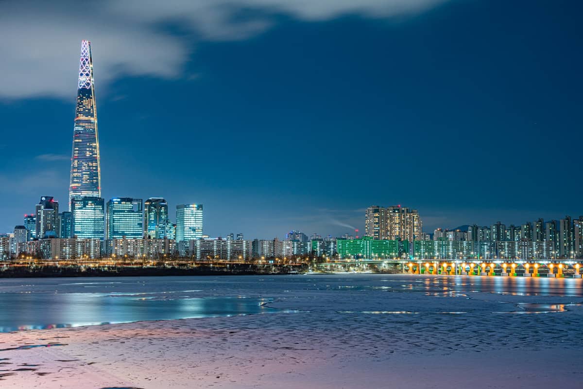 Vista noturna do horizonte de Seul com a Lotte World Tower e as luzes da cidade refletidas no rio Han.