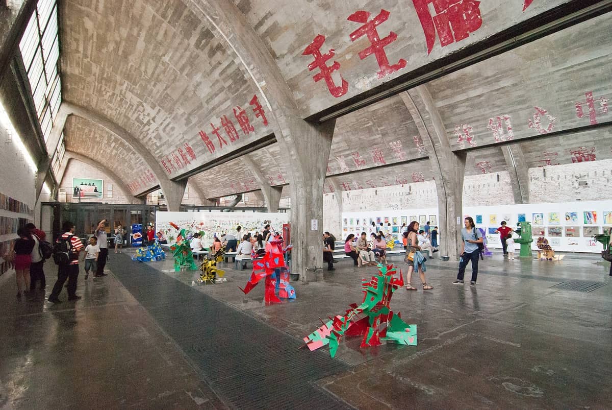 Besucher erkunden die Galerieräume des Kunstviertels 798, mit großen Betonbögen, chinesischen Schriftzeichen, bunten Skulpturen und zeitgenössischen Kunstwerken.