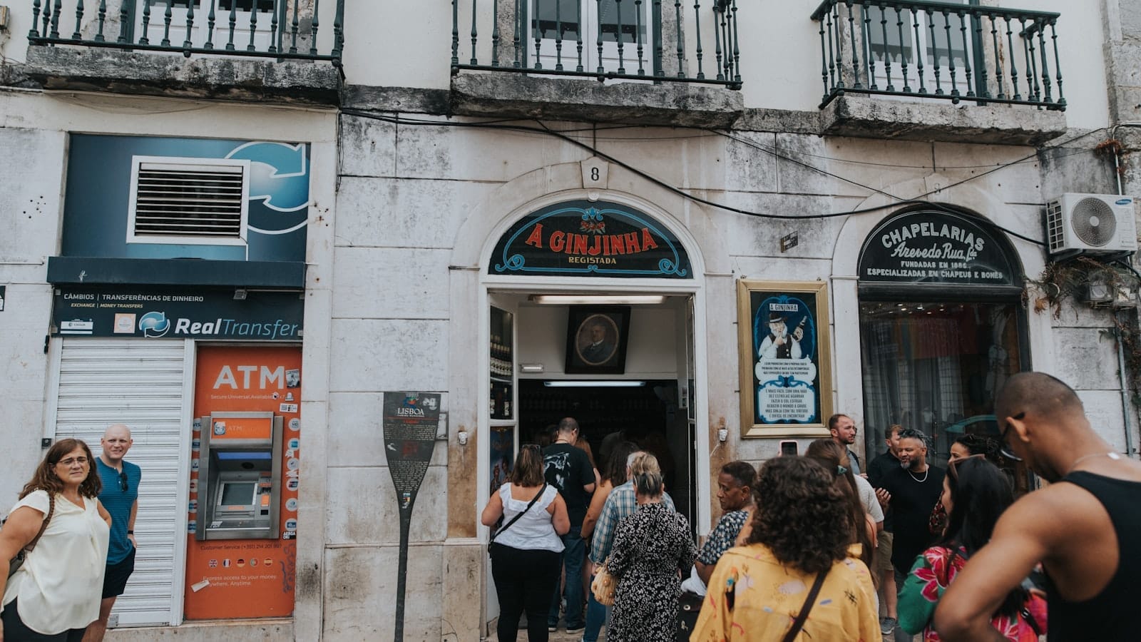 I visitatori si radunano fuori dall'ingresso storico del bar A Ginjinha a Lisbona, con il suo caratteristico insegna e la facciata in pietra ornata ben visibile.