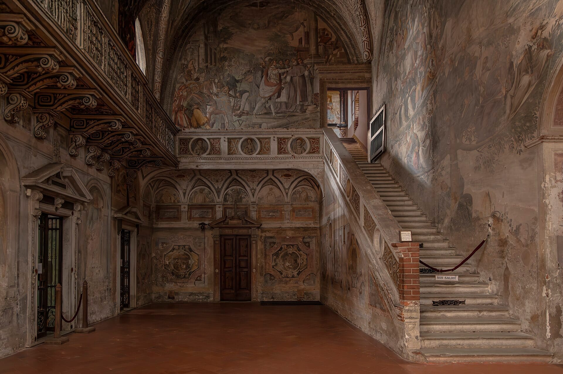 Interno affrescato e ornato con scala in pietra dell'Abbazia di Chiaravalle, con dipinti murali dettagliati, soffitti ad arco e illuminazione ambientale calda.
