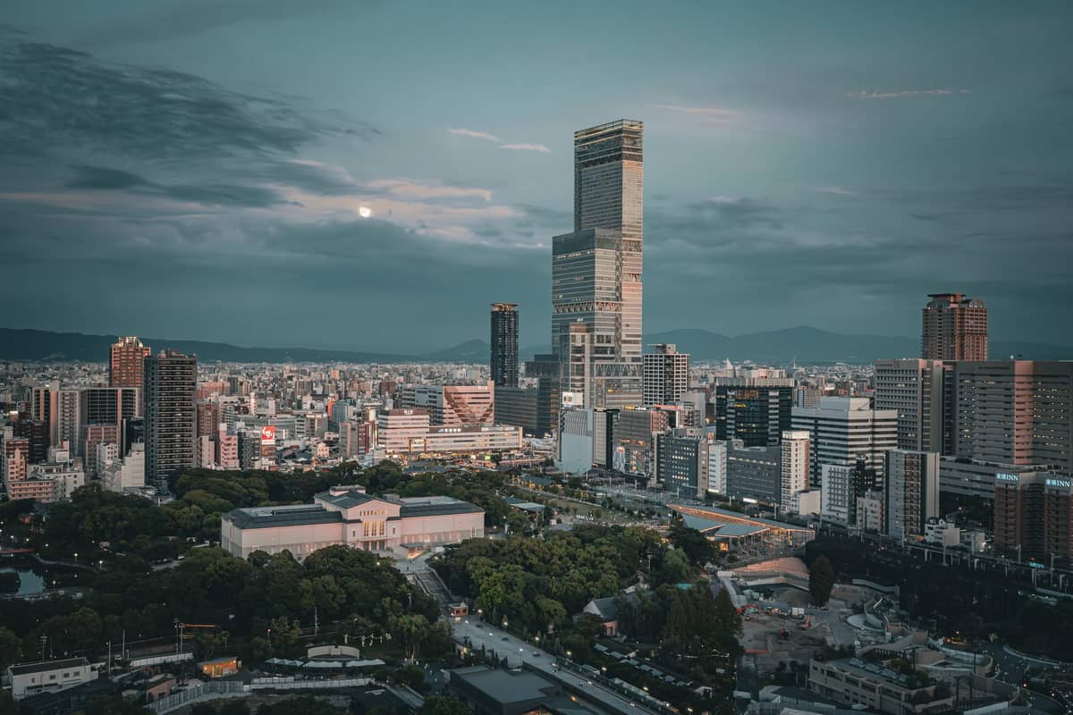 Abeno Harukas towers over the Osaka city skyline at dusk, seen from a distance with the city and distant mountains visible.