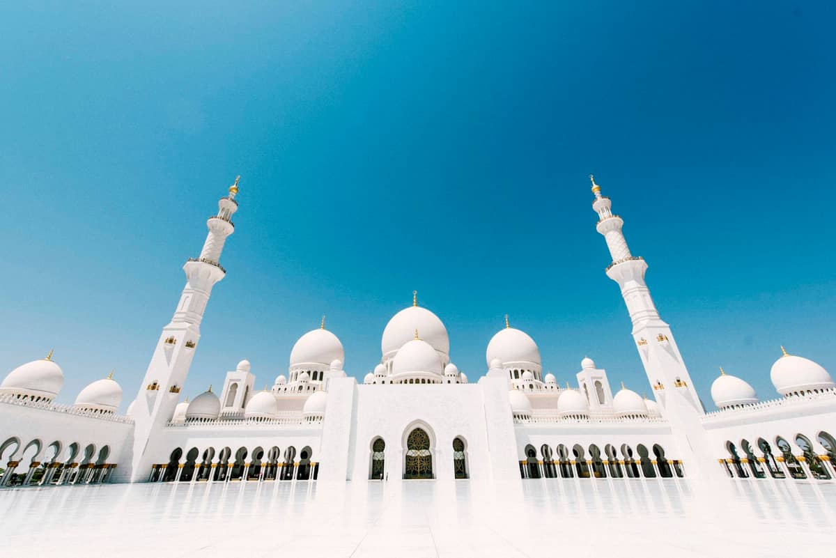 Weitwinkelansicht der Sheikh Zayed Grand Mosque mit ihren großen weißen Kuppeln und Minaretten unter einem strahlend blauen Himmel.