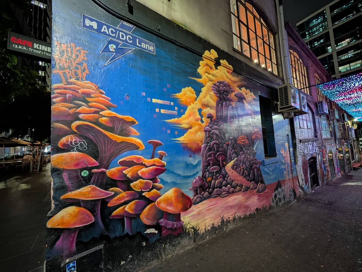 Die AC/DC Lane in Melbourne bei Nacht mit dem blauen Straßenschild und lebhaften Street-Art-Murals an den Backsteingebäuden.