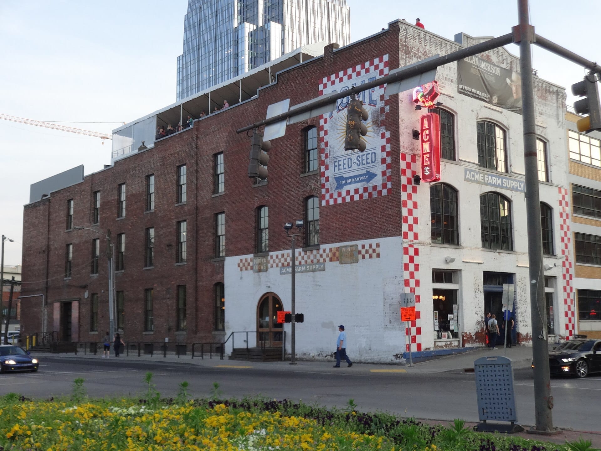 Vista exterior de Acme Feed & Seed, un histórico edificio de ladrillo en Lower Broadway con detalles en rojo, letrero de neón y clientes en la azotea al atardecer.