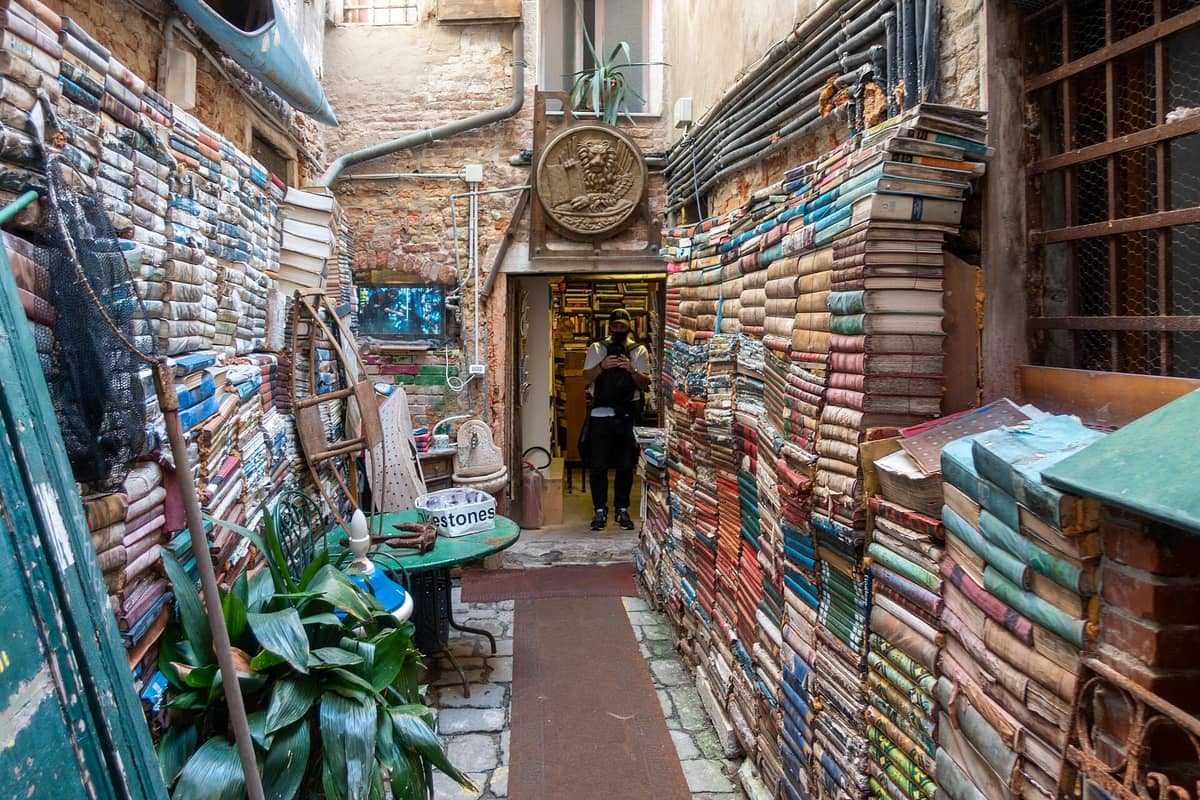 Der berühmte Außengang der Libreria Acqua Alta in Venedig mit farbenfrohen Stapeln alter Bücher, die den Eingang vor Überschwemmungen schützen, und dem Schild der Buchhandlung über dem Eingang.