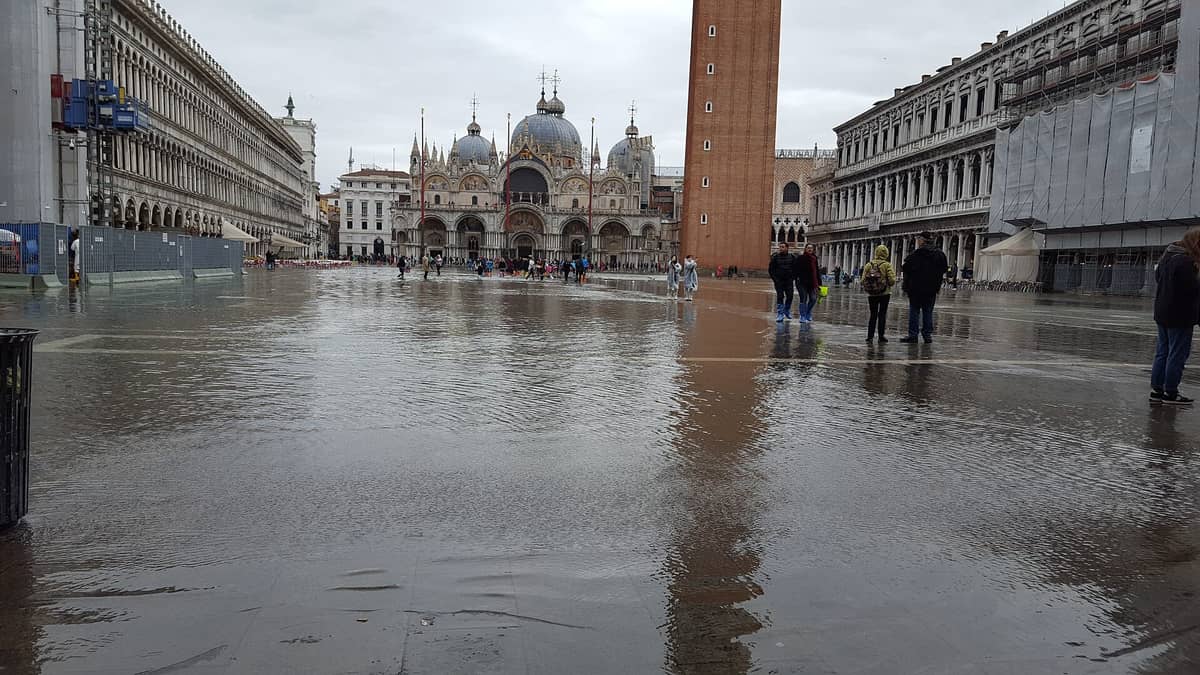 Piazza San Marco in Venedig während der Acqua alta teilweise überflutet, mit flachem Wasser auf dem Platz und Menschen in Gummistiefeln.