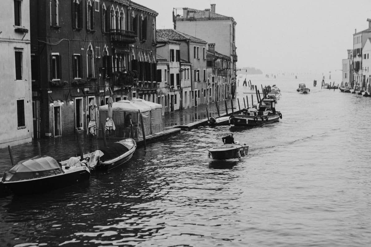 Venezianischer Kanal mit teilweise überschwemmtem Gehweg, Booten und steigendem Wasserstand, der typische Acqua-alta-Bedingungen zeigt