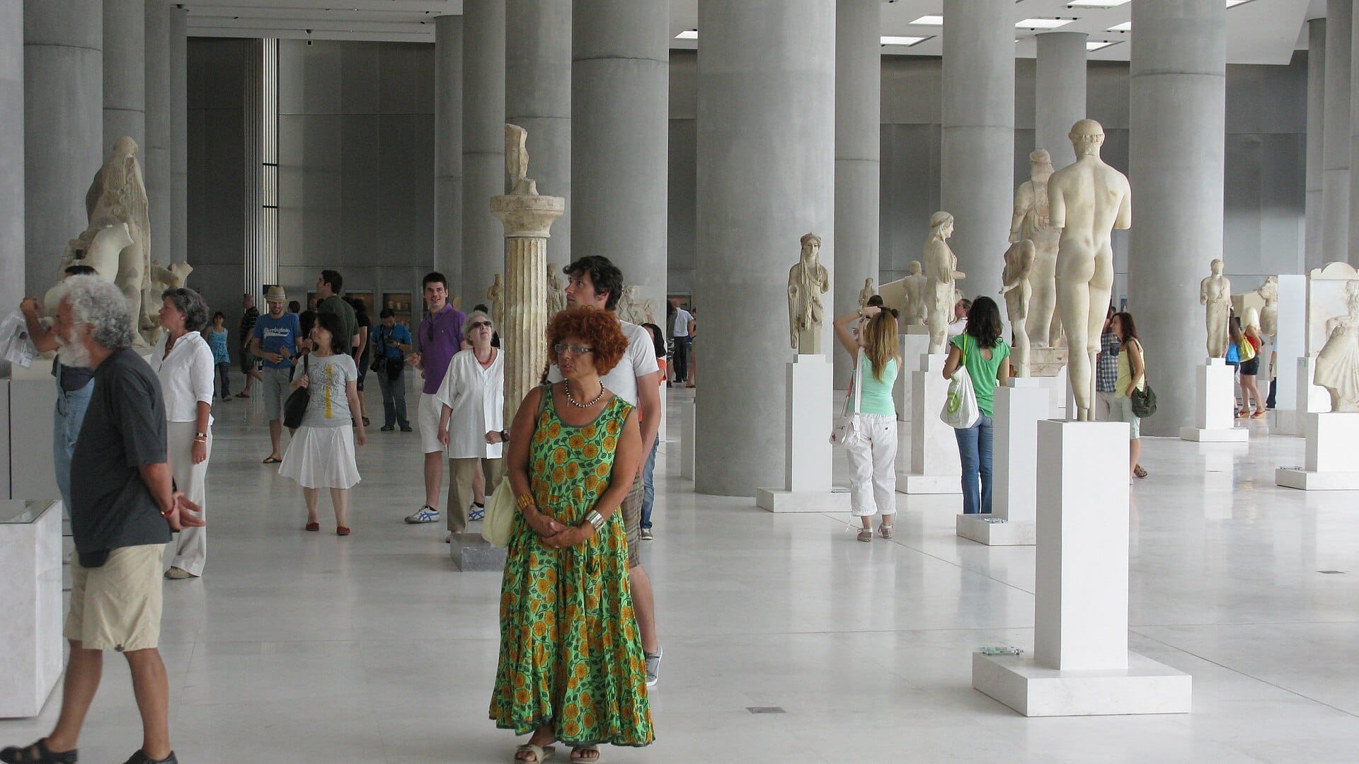 I visitatori camminano tra antiche statue greche nella luminosa e spaziosa galleria principale dell'Acropolis Museum ad Atene.