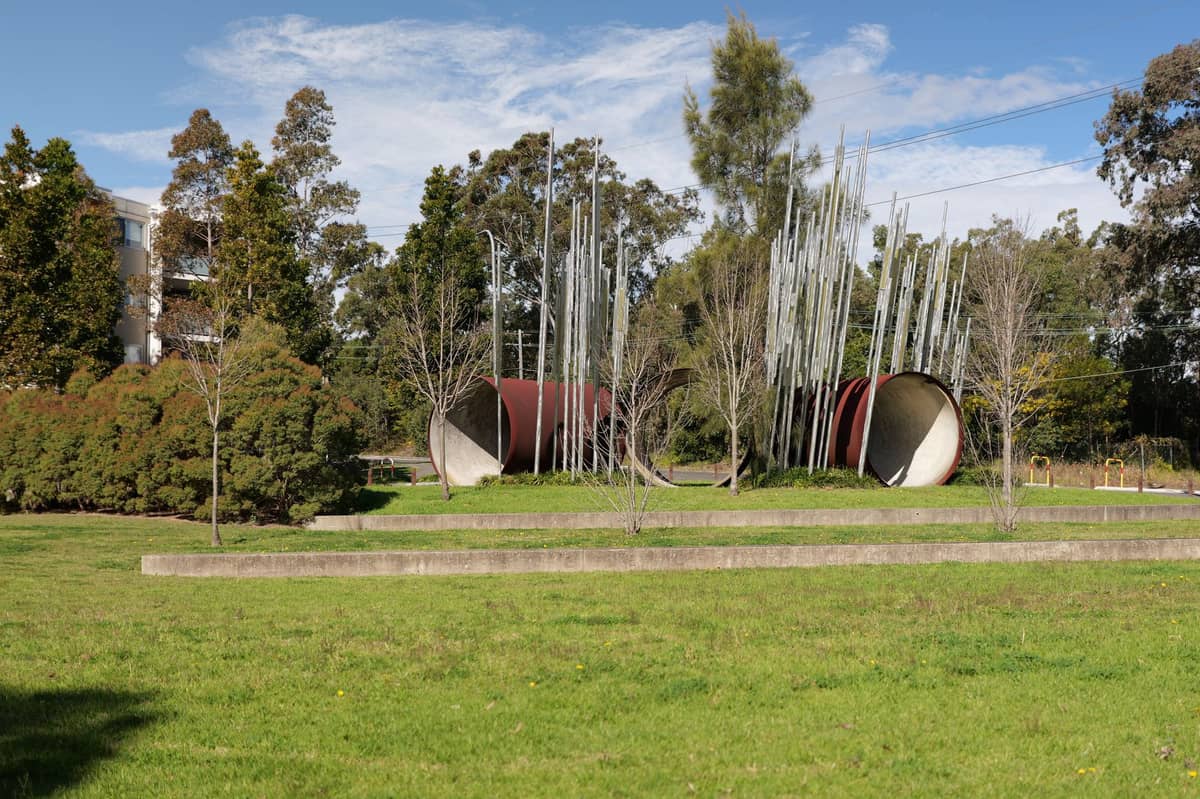 Kunstinstallation im Freien mit hohen Metallstangen und zylindrischen Strukturen, umgeben von Gras und Bäumen im Warriparinga Reserve.
