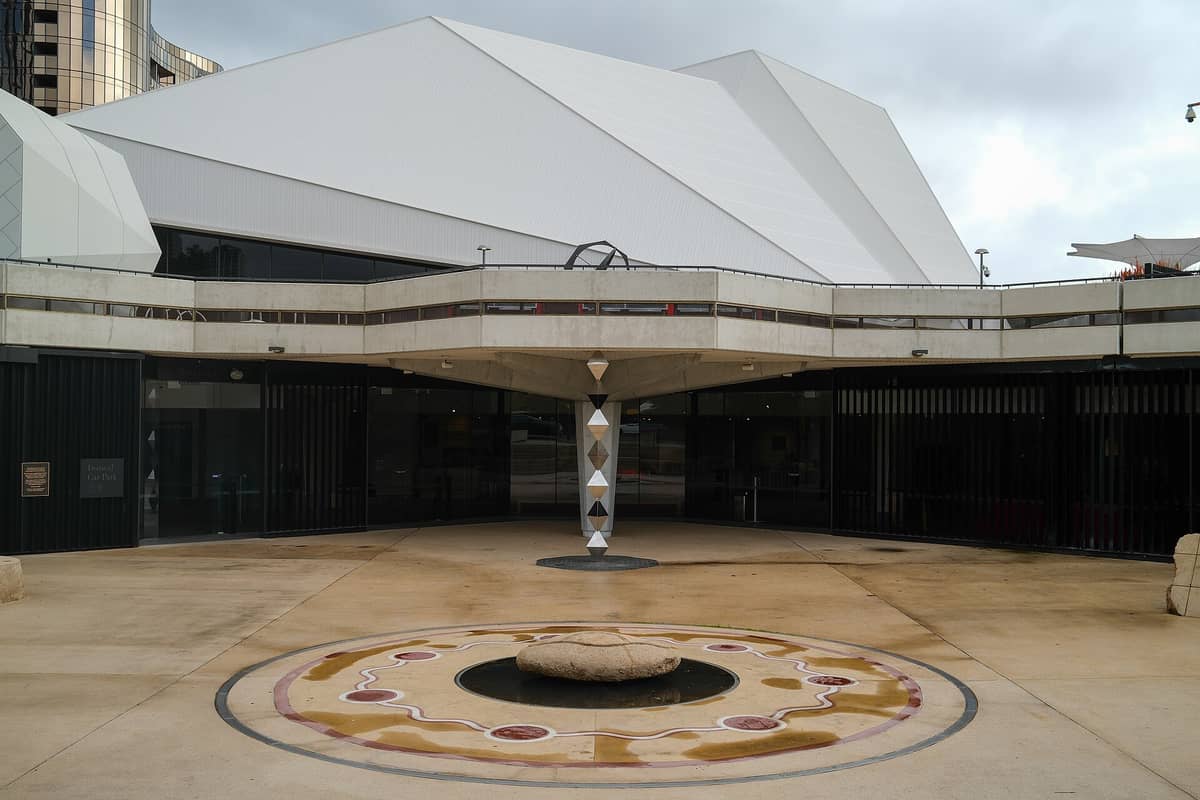 Frontansicht des Adelaide Festival Centre mit seinem markanten weißen geometrischen Dach und dem Eingangsplatz mit einem runden Mosaikbrunnen.