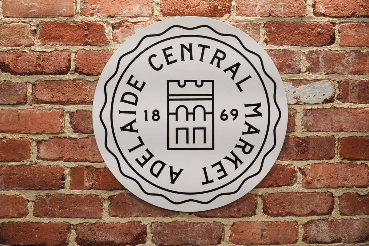 Okrągły znak z emblematem Adelaide Central Market na ceglanej ścianie z nazwą i rokiem 1869.