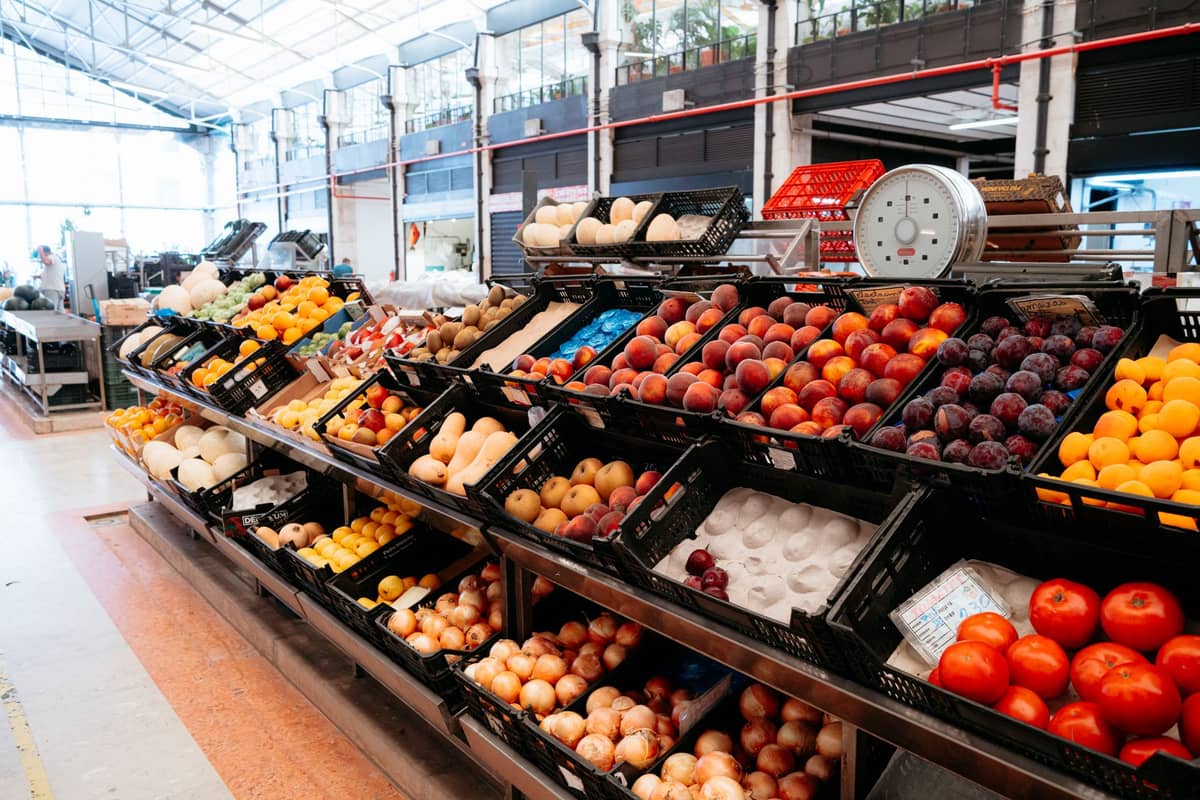 Szeroki widok na stoisko ze świeżymi produktami w krytym targu z brzoskwiniami, śliwkami, cebulą, pomidorami i innymi sezonowymi owocami i warzywami.