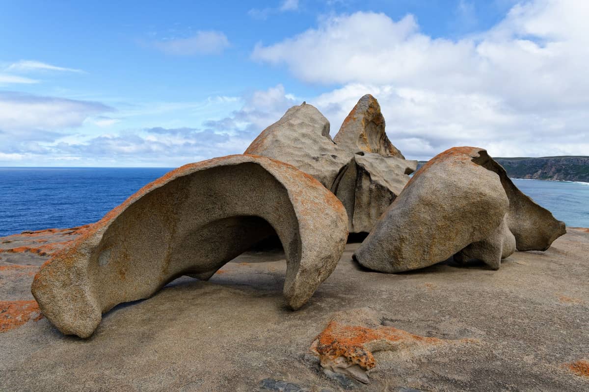 Große glatte Granitfelsen, bekannt als Remarkable Rocks, auf einem Küstenkap, mit Ozean und Klippen in der Ferne unter einem blauen Himmel.
