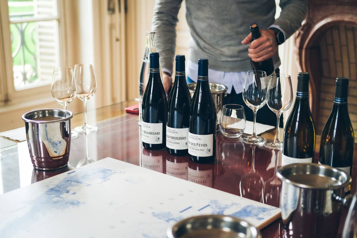 Person presenting a curated wine tasting with several bottles and empty glasses on a polished table in a refined, bright room