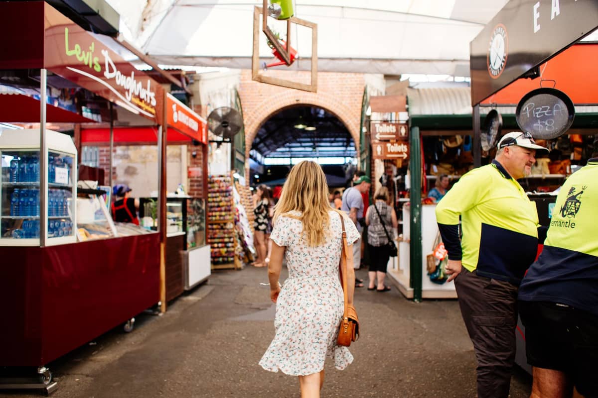 People walking through covered market stalls with food and artisanal products at the Adelaide Central Market.
