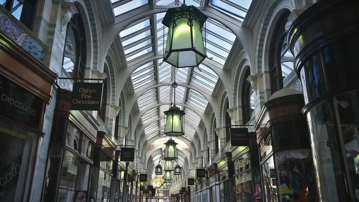 Victorian-style shopping arcade with ornate glass roof, hanging lanterns, and specialty shop signs, evoking Adelaide's historic architectural shopping experience.