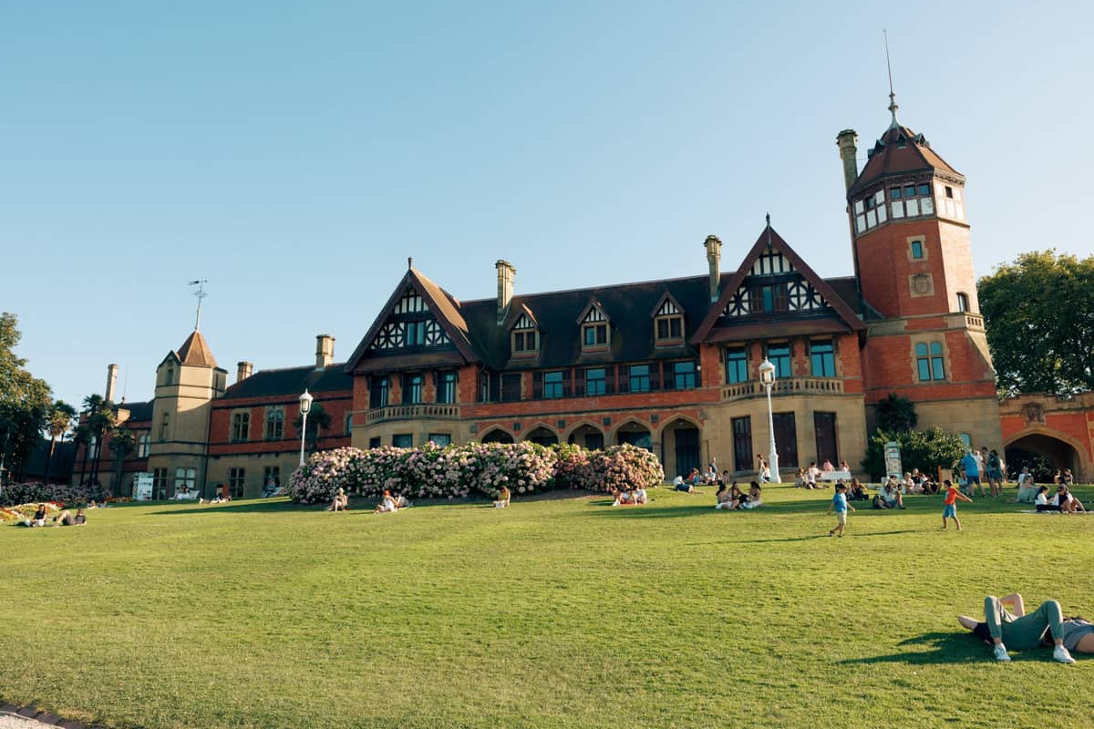 Large historic building with lawn and families relaxing outside on a sunny day, likely a landmark park in Adelaide.