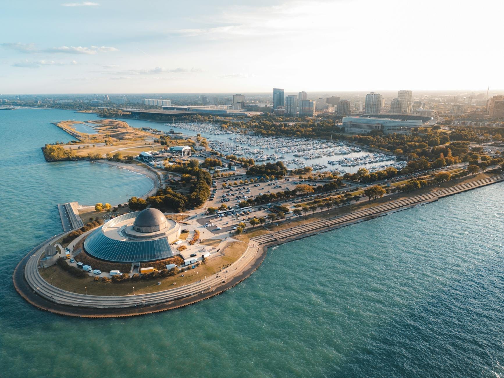 Vista aerea dell'Adler Planetarium in punta a una penisola, circondato dal lago Michigan con lo skyline di Chicago sullo sfondo in una giornata di sole.