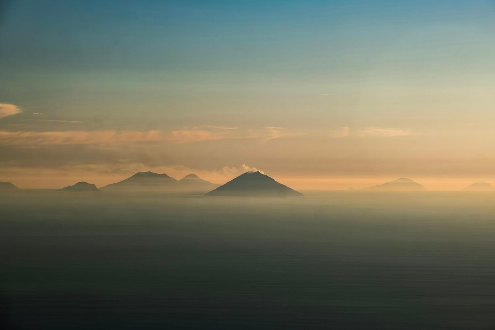 Dramatischer Blick auf mehrere Äolische Inseln mit Vulkangipfeln, die bei Sonnenuntergang aus dem dunstigen Meer ragen – eine traumhafte Atmosphäre.