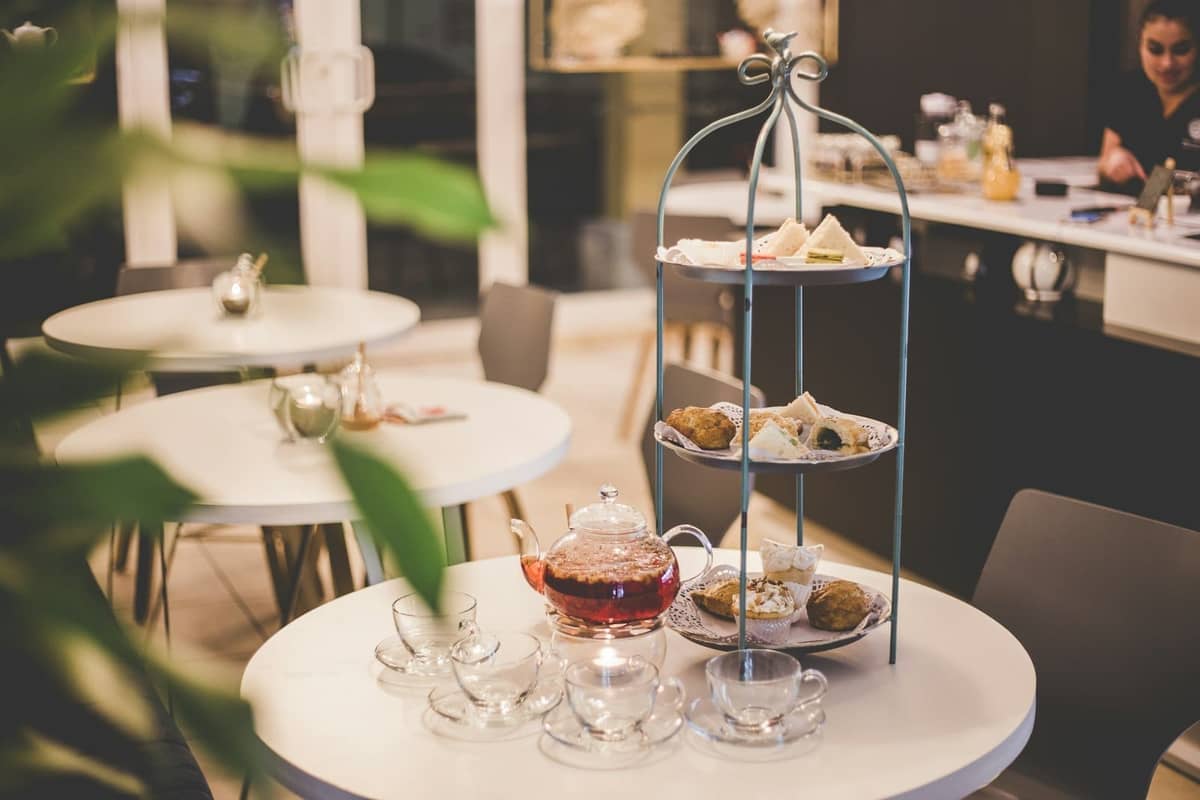 Mesa de café moderno em Londres preparada com torre de chá da tarde, bule e xícaras de chá, em um ambiente relaxado e bem iluminado.