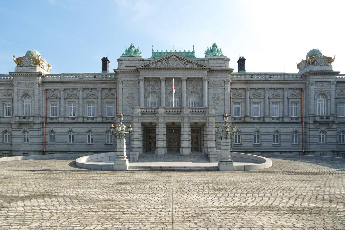 Front view of Akasaka Palace in Tokyo, showcasing its grand neo-baroque European-style architecture with ornate stonework, columns, and decorative roof features under a clear sky.