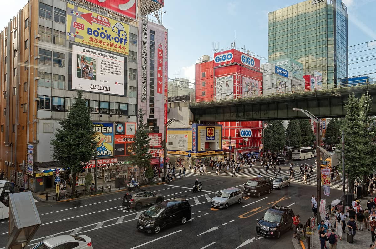 Akihabara Electric Town intersection with crowds, colorful billboards, anime advertisements, and Chuo-dori under an overhead railway, capturing the vibrant heart of Akihabara.