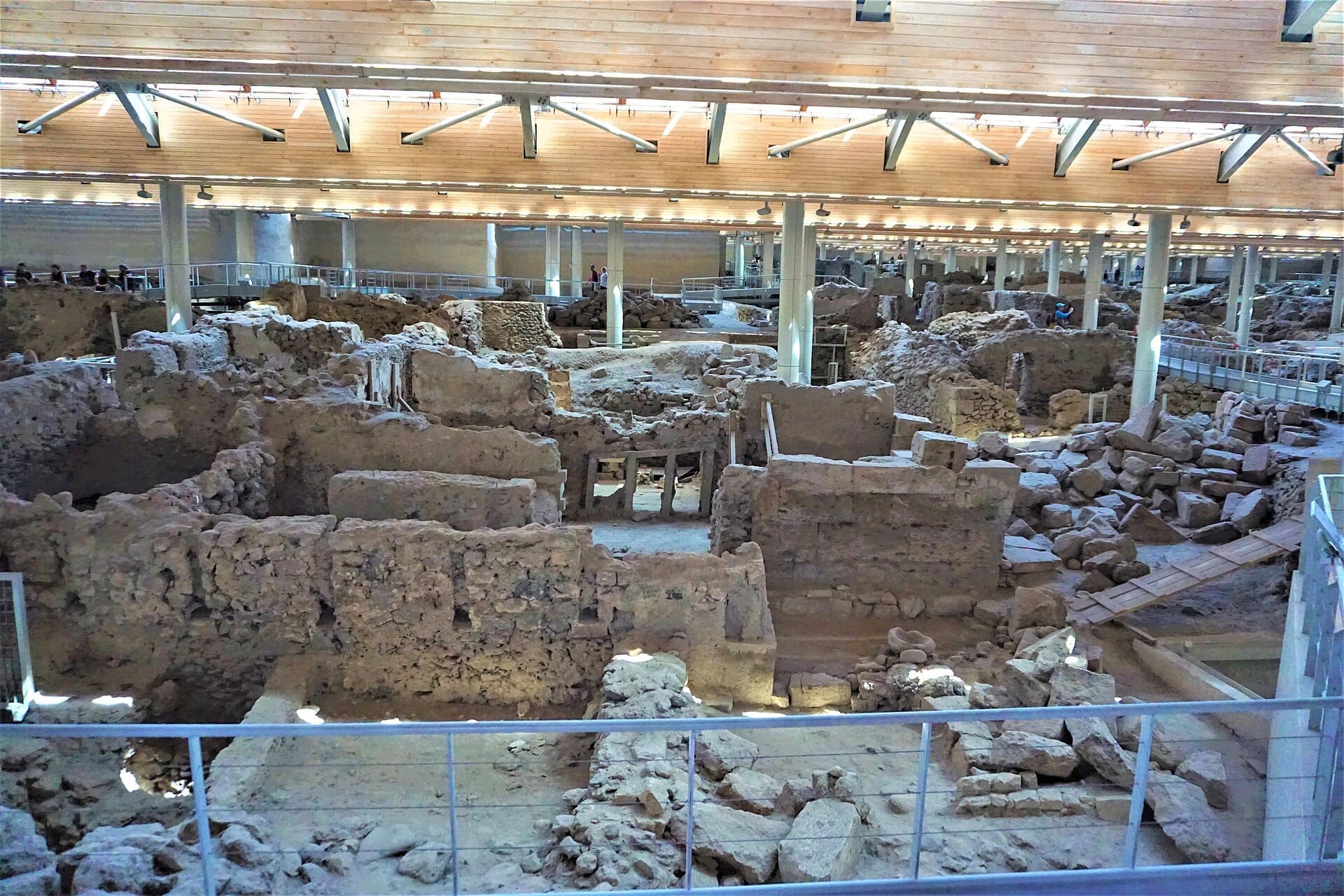 ภาพรวมของแหล่งโบราณคดี Akrotiri ที่แสดงซากปรักหักพังหินโบราณ ทางเดิน และหลังคาไม้สมัยใหม่เพื่อการป้องกันใน Santorini