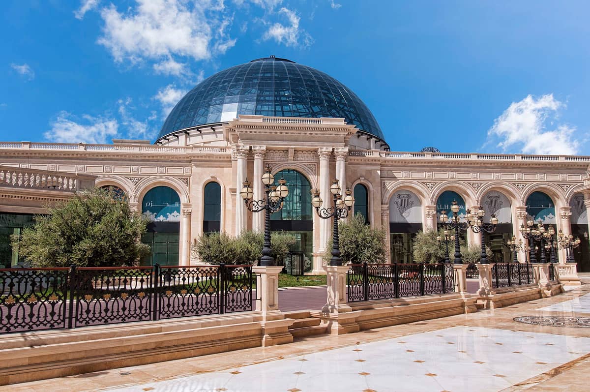 Außenansicht des Al Hazm Mall in Doha mit seinem imposanten Kuppeldach, verzierten klassischen Säulen und eleganter Steinfassade unter blauem Himmel.