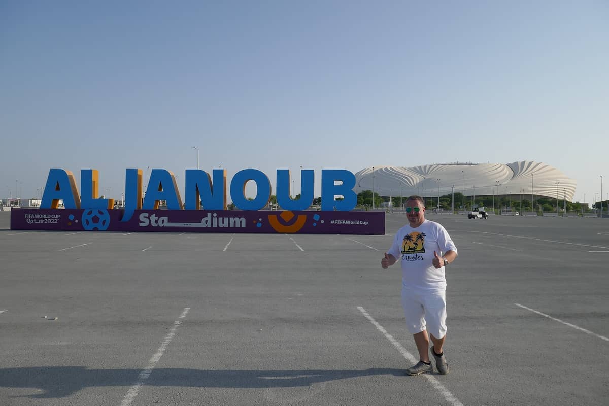 Das Al Janoub Stadion in Al Wakrah, Katar, hinter einem großen, bunten Schild und einem Besucher auf einem sonnigen, leeren Parkplatz.