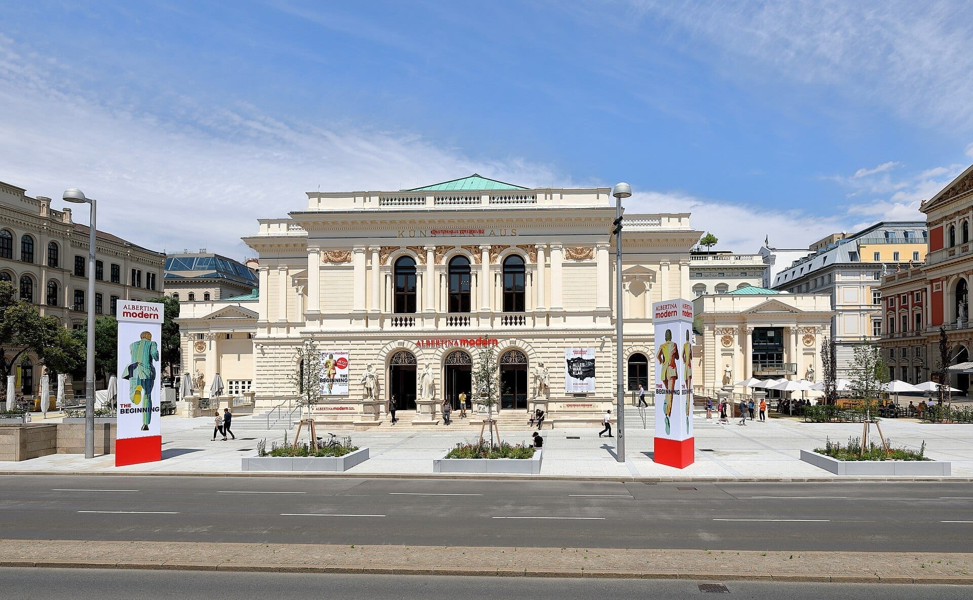 Albertina Modern am Karlsplatz in Wien, mit ihrer imposanten historischen Fassade, lebhaften Bannern und Menschen, die an einem sonnigen Tag spazieren.