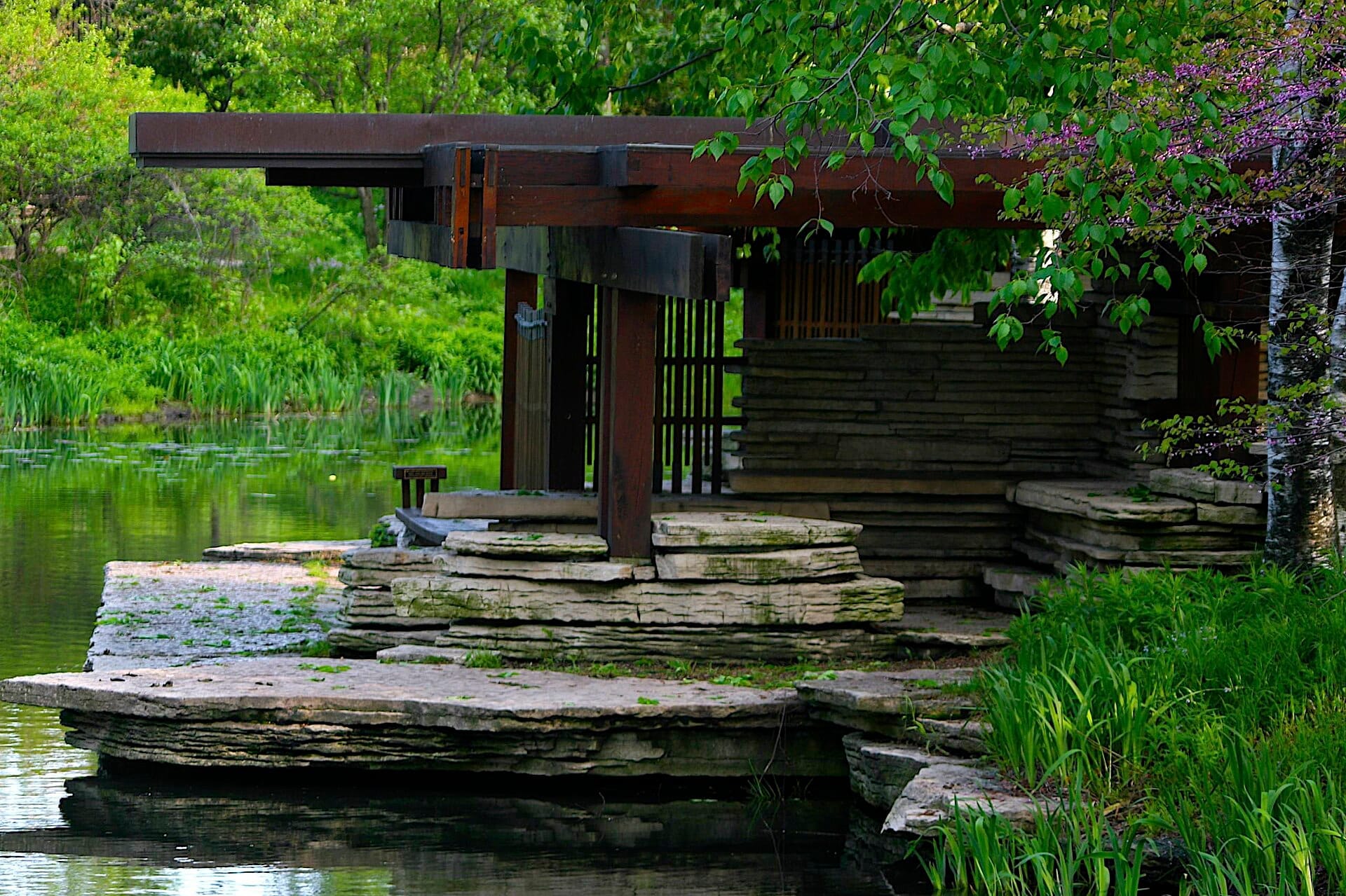 Padiglione in pietra in stile Prairie accanto a uno stagno tranquillo, circondato da rigogliosa vegetazione all'Alfred Caldwell Lily Pool nel Lincoln Park di Chicago.