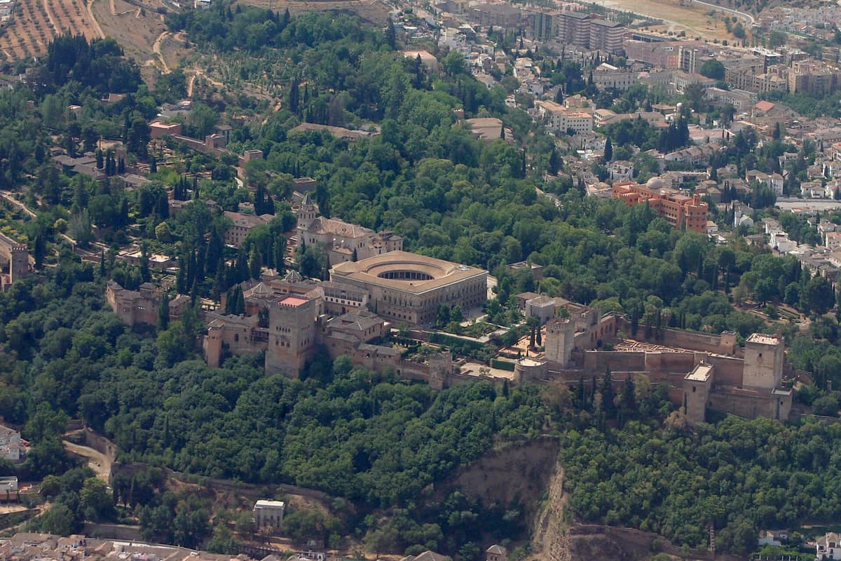 มุมมองทางอากาศของกลุ่มอาคาร Alhambra ในเมือง Granada ประเทศสเปน ล้อมรอบด้วยต้นไม้หนาแน่นและอาคารในเมืองเป็นฉากหลัง