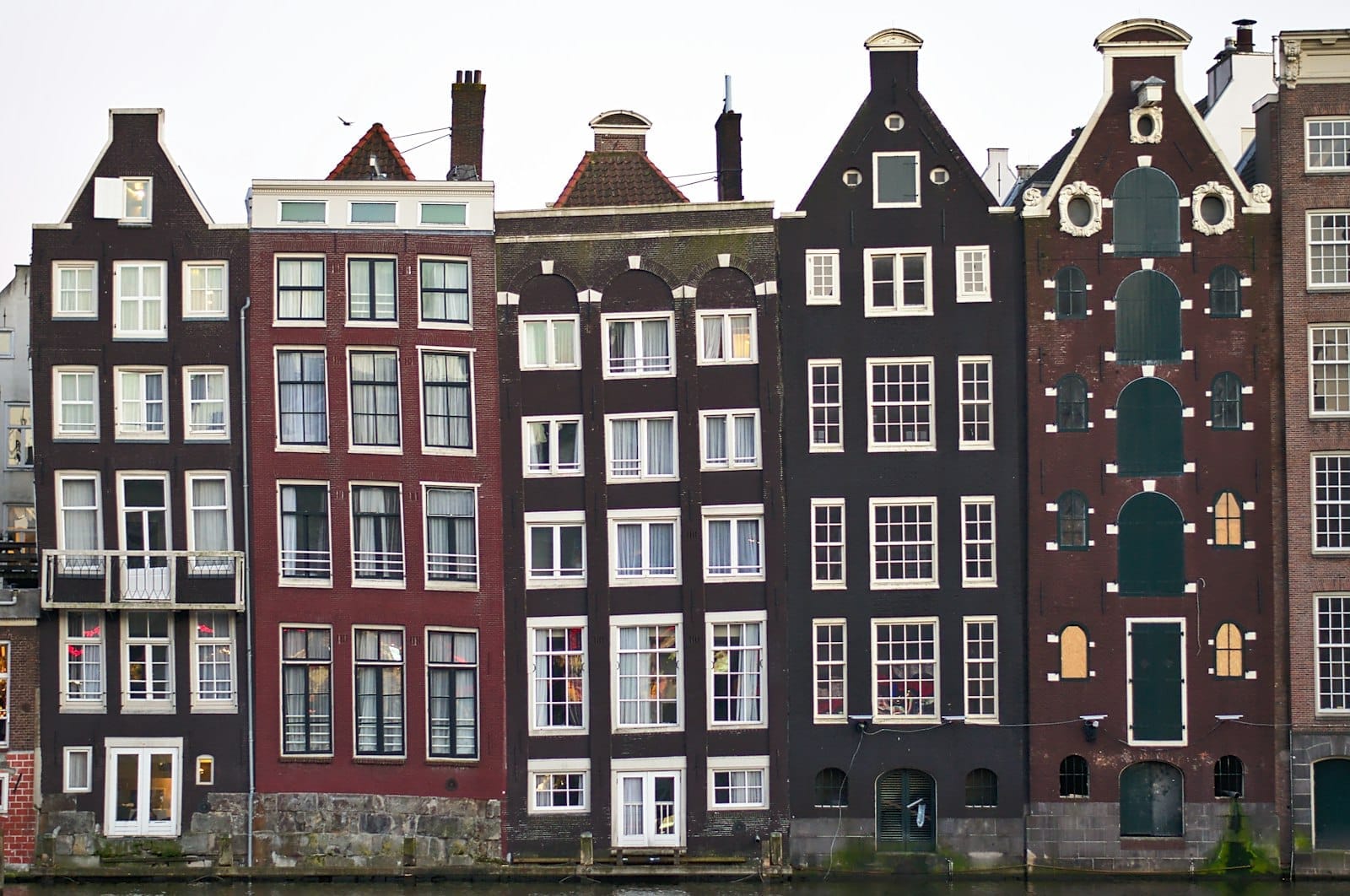 Vista de cerca de las casas del canal de Ámsterdam con fachadas estrechas y altas y frontones variados reflejados en el agua.