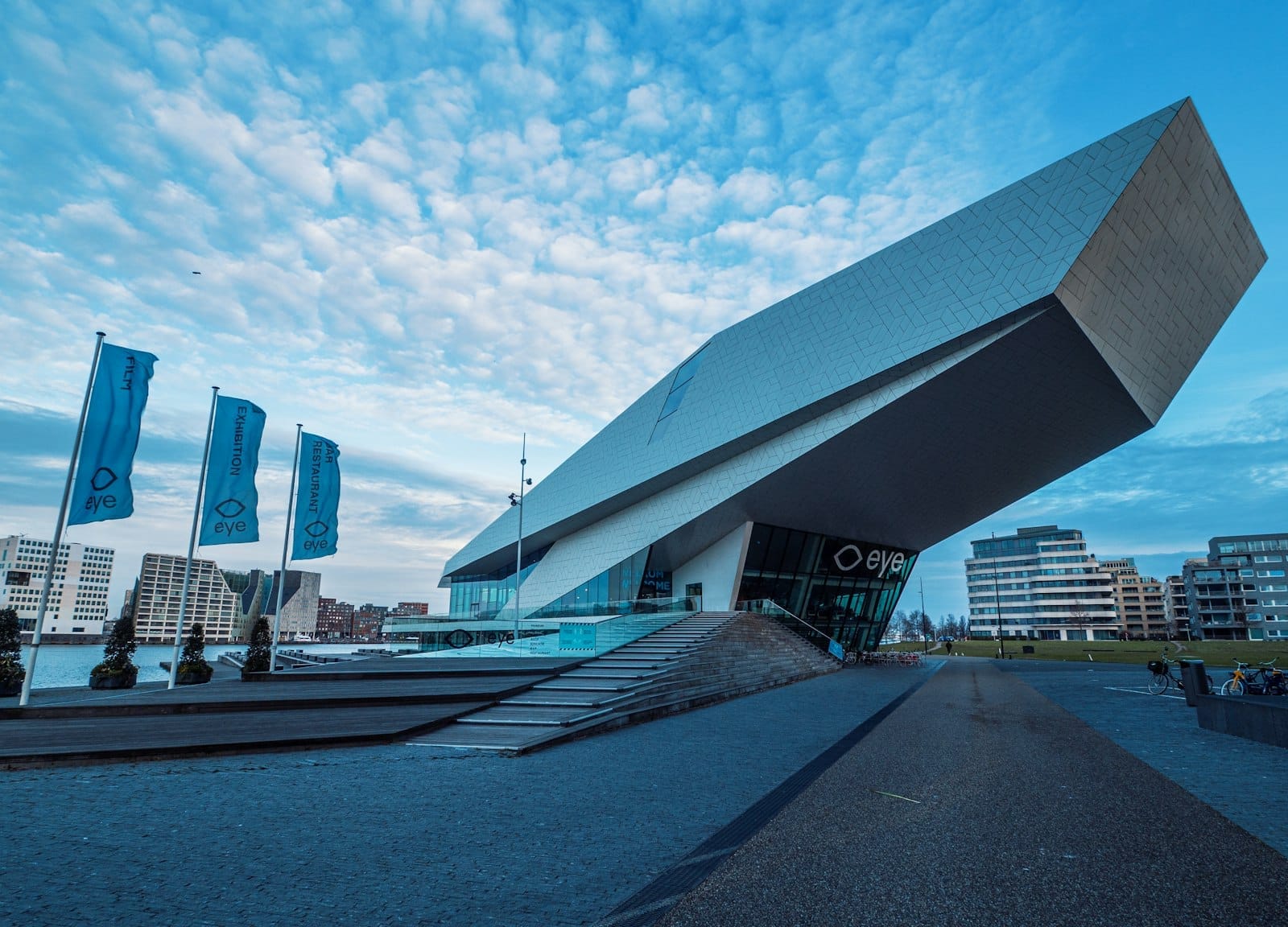 Impresionante arquitectura moderna del Eye Filmmuseum en el frente acuático IJ de Ámsterdam, con su fachada blanca angular y los edificios contemporáneos circundantes bajo un cielo azul.