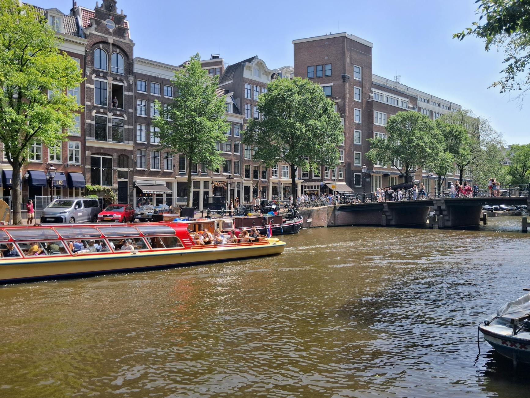 Cảnh kênh đào nắng đẹp ở Amsterdam với thuyền du lịch, những ngôi nhà Hà Lan cổ điển và mọi người tận hưởng thời tiết ấm áp trên cầu.