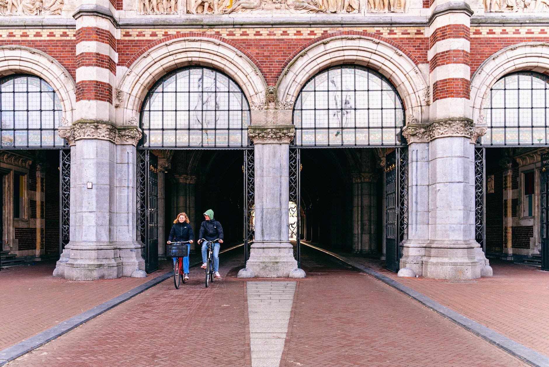 Hai người đạp xe đi qua dưới mái vòm arcade của Rijksmuseum ở Amsterdam, một địa danh mang tính biểu tượng trên Museumplein.