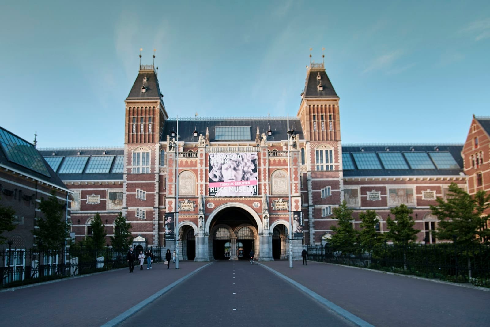 Góc nhìn rộng về lối vào Rijksmuseum ở Amsterdam, với nhiều người đi bộ phía trước vào một ngày trời trong xanh.