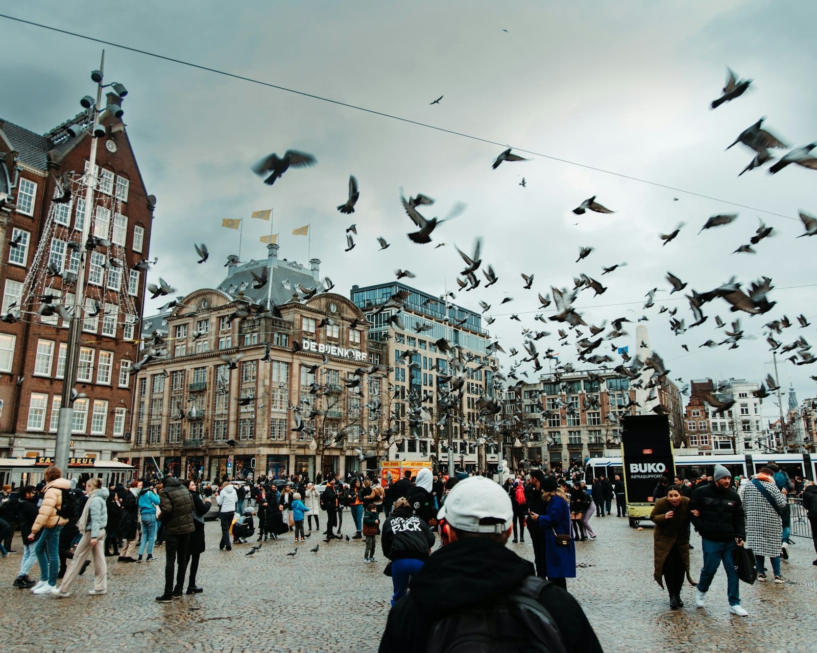 Concurrida Plaza Dam en Ámsterdam con multitudes, palomas y edificios históricos. Escena urbana que muestra una popular zona central afectada por las nuevas normas sobre el tabaco.