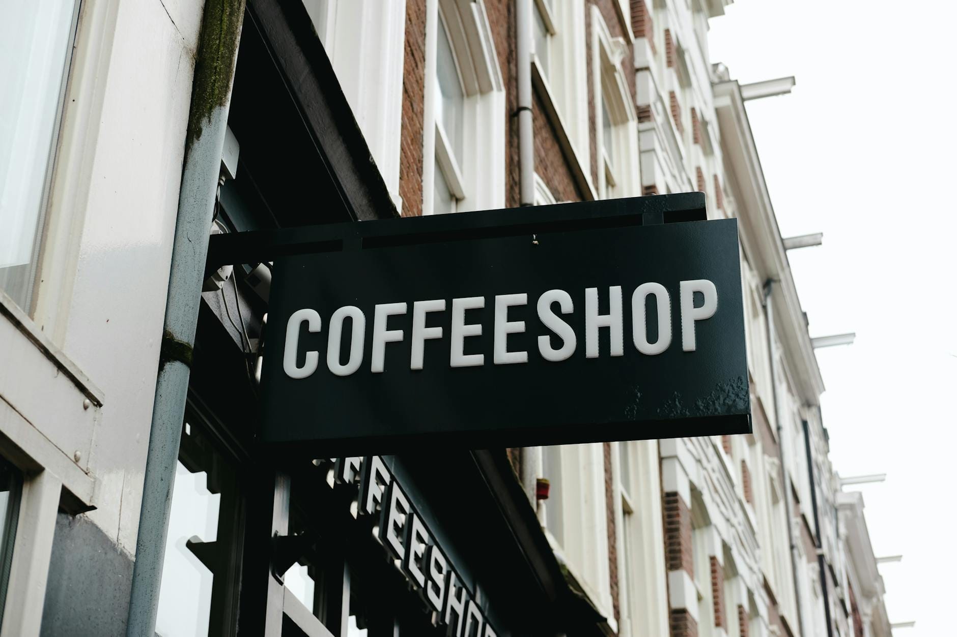 Vista de la calle de un edificio en Amsterdam con un letrero negro que dice 'COFFEESHOP' en grandes letras blancas.
