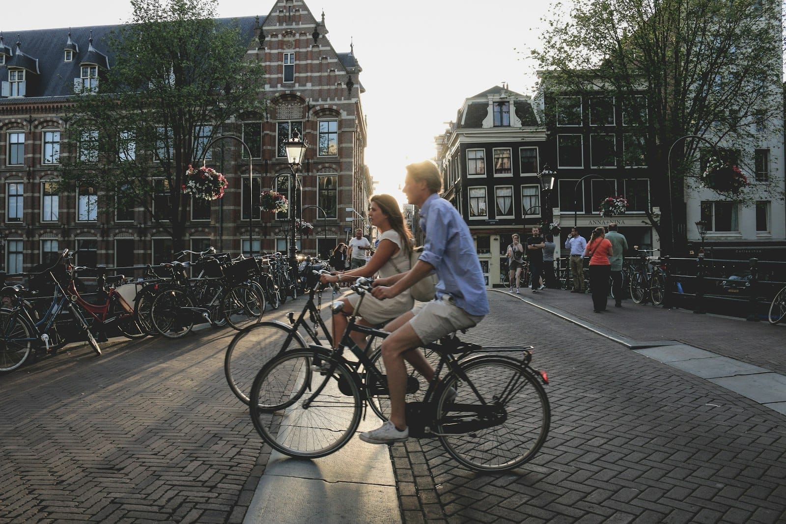 Una pareja montando bicicletas juntos en una pintoresca calle de Amsterdam con edificios históricos y bicicletas al atardecer.