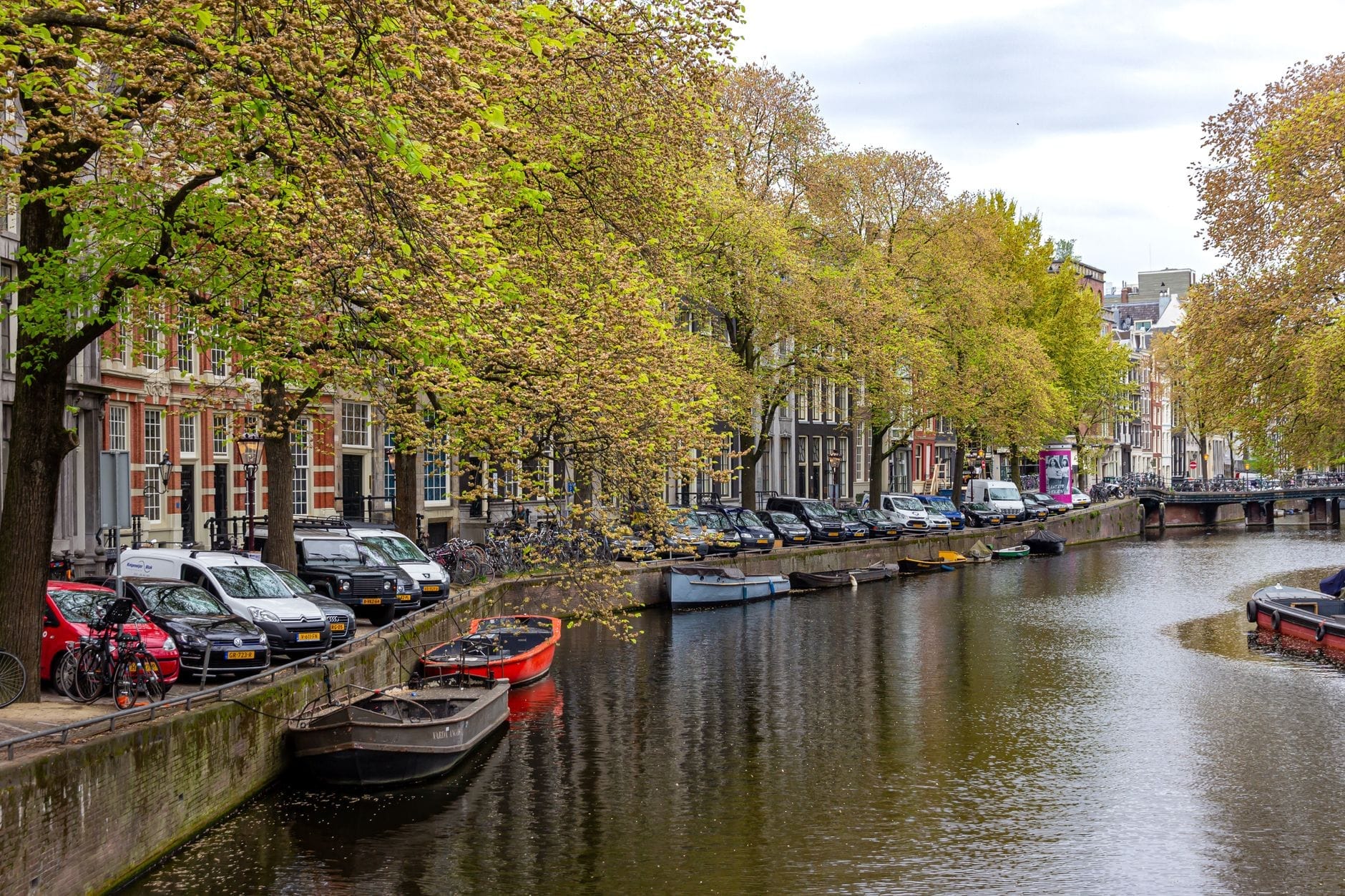 Canal de Ámsterdam bordeado de árboles con barcas amarradas y casas históricas, creando una escena de barrio tranquila y romántica para que las parejas exploren.