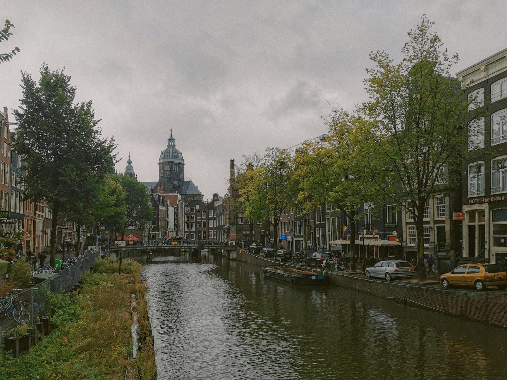 Día de otoño nublado en Ámsterdam con cielos cubiertos, vista al canal, edificios históricos y árboles con follaje de principios de otoño.