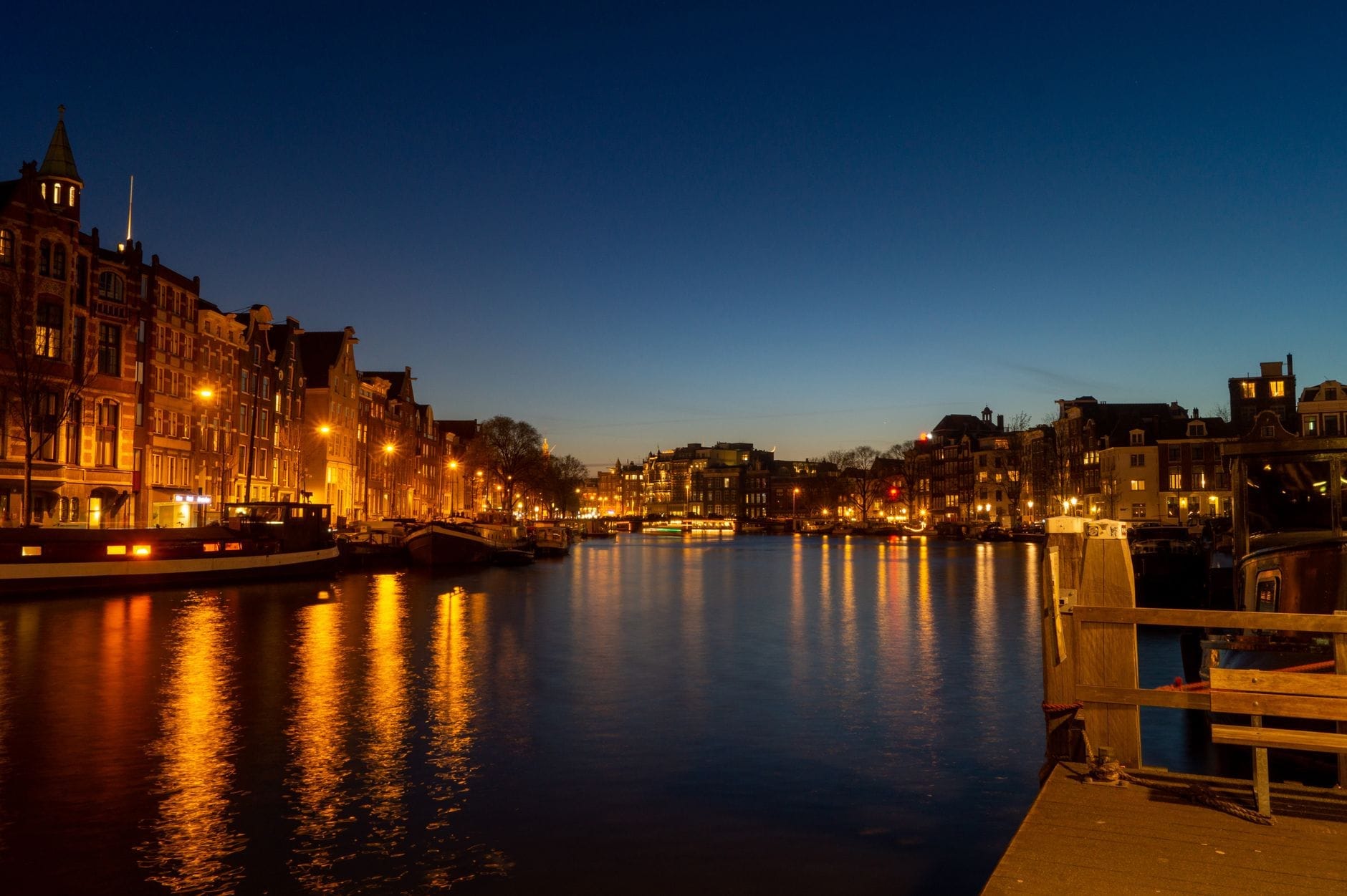 Canal de Ámsterdam al atardecer con luces festivas reflejadas en el agua tranquila y edificios históricos que crean una atmósfera mágica de invierno.