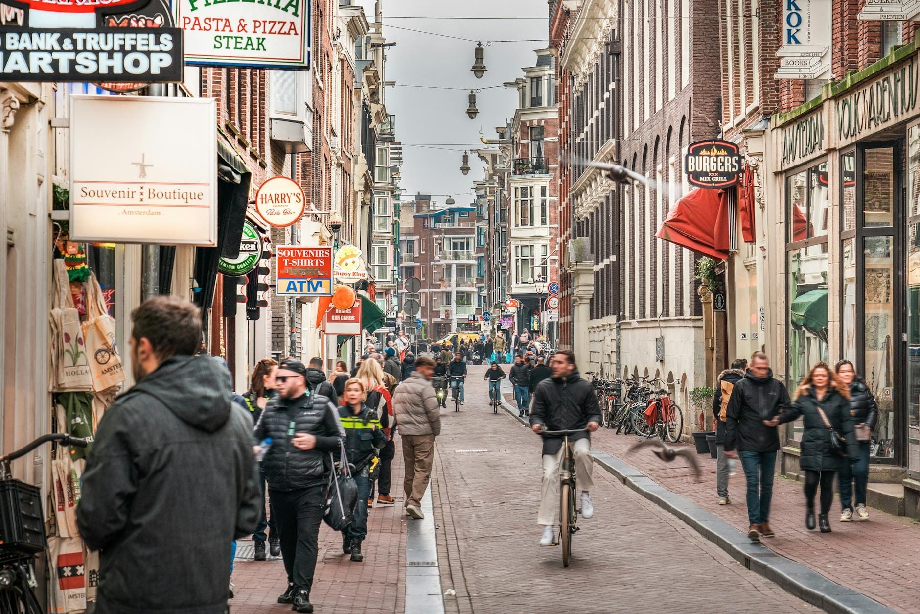 Concurrida calle de Ámsterdam bordeada de tiendas, ciclistas y peatones en un nublado día de invierno.