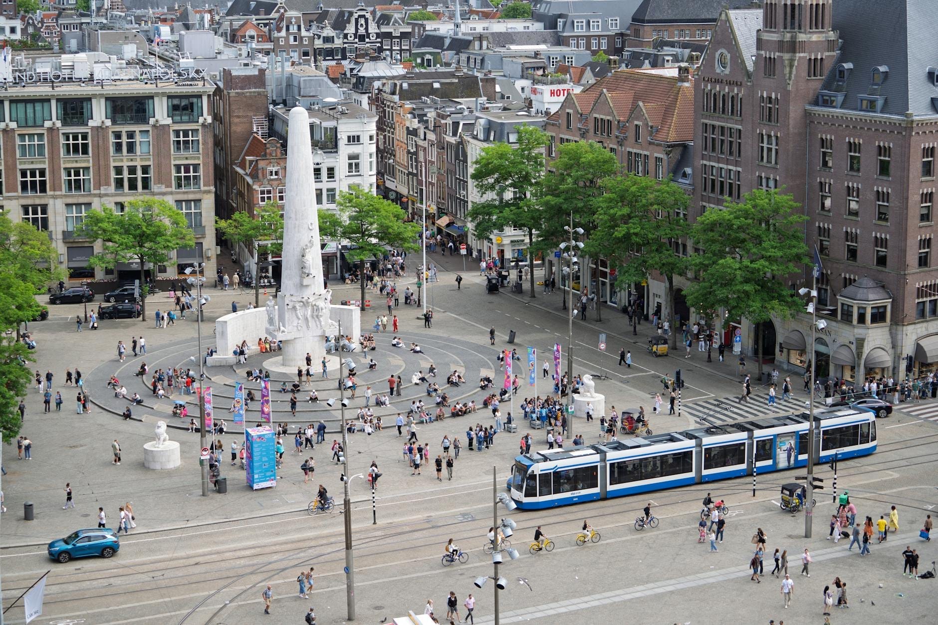 Vista aérea de la Plaza Dam en Ámsterdam con el Monumento Nacional, un tranvía y personas paseando por la plaza abierta.