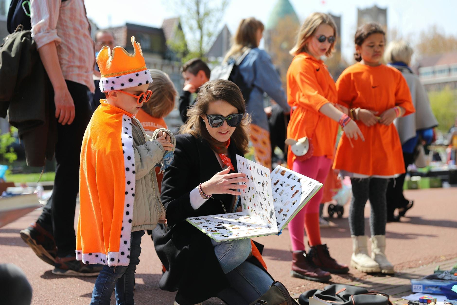 Personas con ropa naranja comprando y vendiendo artículos al aire libre, probablemente durante las festividades del Día del Rey en Amsterdam.