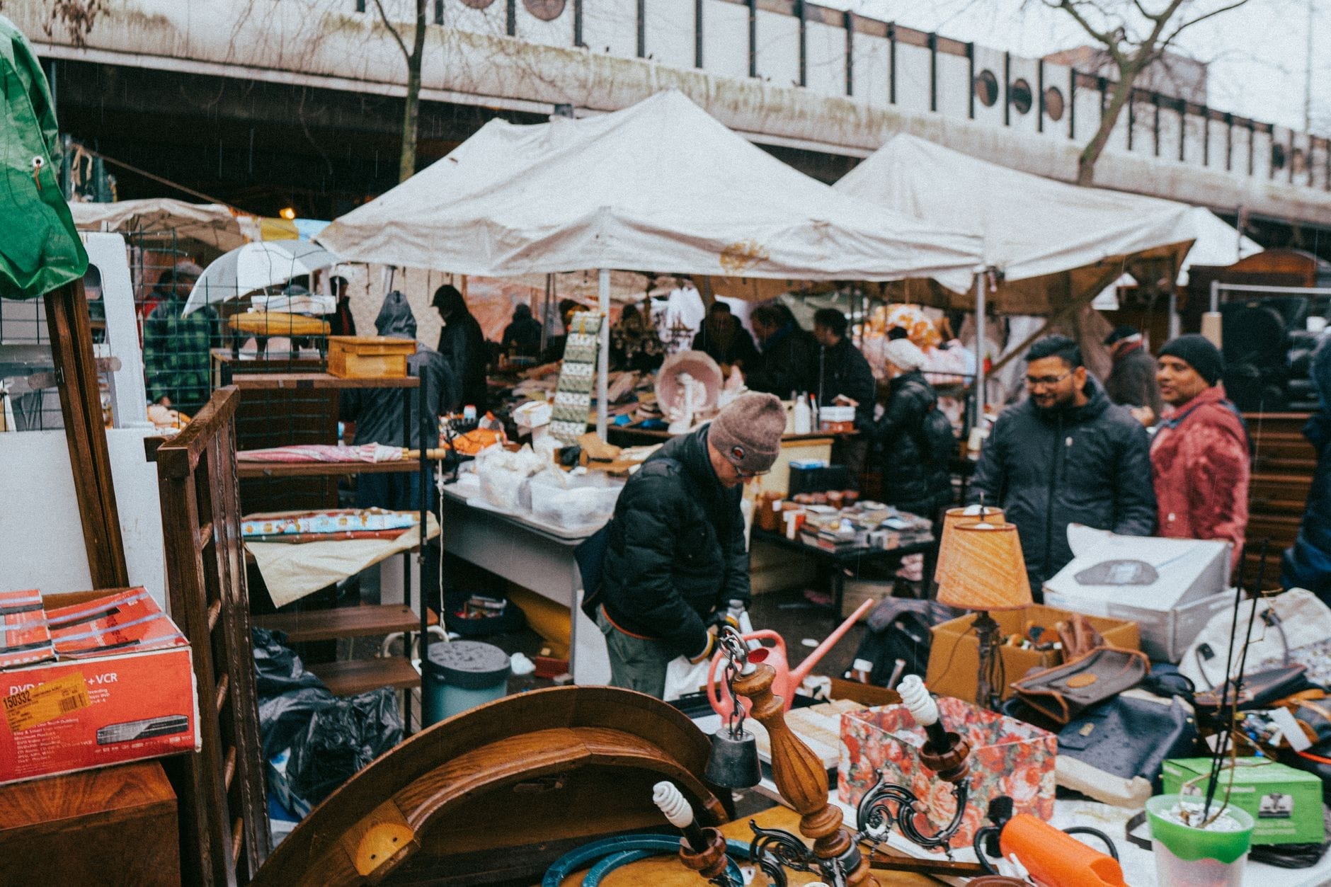 Chợ đồ cũ ngoài trời nhộn nhịp ở Amsterdam, với người mua sắm đang xem hàng secondhand và đồ cổ dưới những chiếc lều trắng.